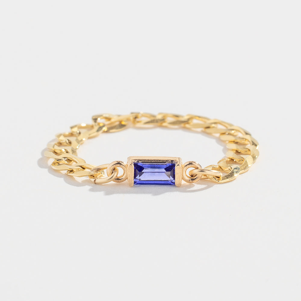 Gold chain ring with a rectangular blue gemstone centerpiece on a plain white background