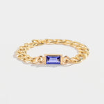 Gold chain ring with a rectangular blue gemstone centerpiece on a plain white background