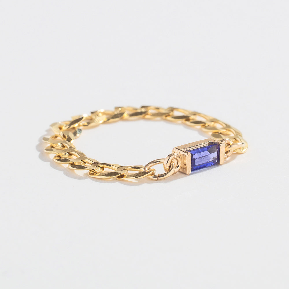 Gold chain ring with a rectangular blue gemstone centerpiece on a plain white background