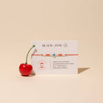 Red bracelet with white description card on beige background reads "power and courage - groundedness and trust - self confidence - increased energy"