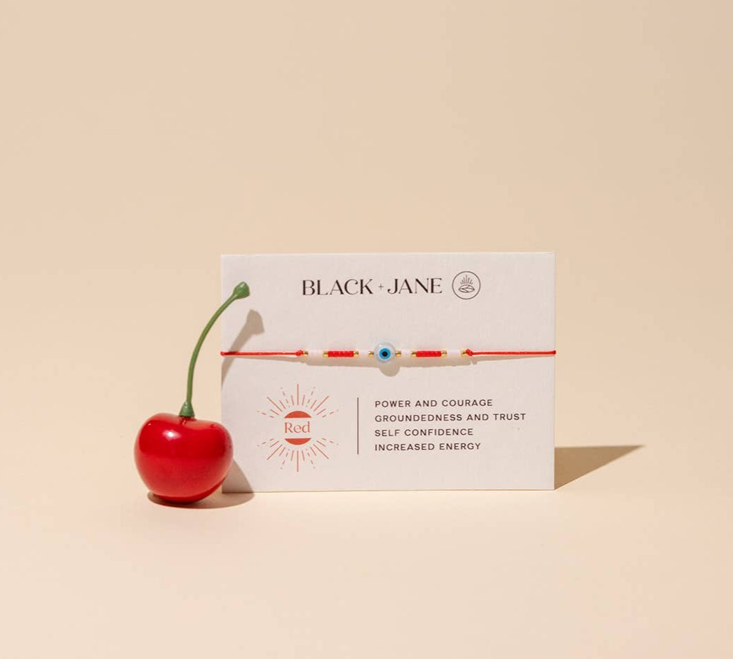 Red bracelet with white description card on beige background reads "power and courage - groundedness and trust - self confidence - increased energy"