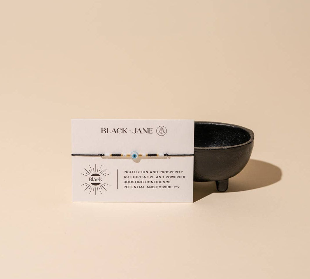 Black bracelet with white description card on beige background reads "protection and prosperity - authoritative and powerful - boosting confidence - potential and possibility" 